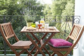 A wooden table with a potted plant, a bottle, and a glass on a balcony with wrought iron railings.