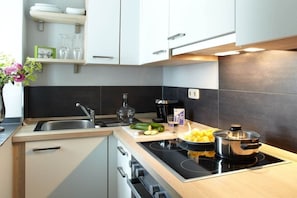 A modern kitchen with a black stovetop, a sink, and a countertop with a cutting board, a pot, and some vegetables.