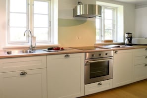 A kitchen with a stainless steel range, a double oven, a sink, and a window with a view of greenery. - Old Shoemaker's House (Stenderup bei Gelting)