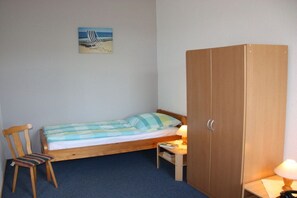 Ein Einzelbett mit gestreifter Decke, ein Holzschrank, ein Stuhl, ein kleiner Tisch mit einer Lampe und ein Bild an der Wand.