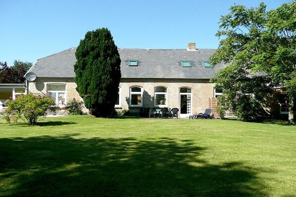 A two-story house with a well-maintained lawn, a large tree, and a patio with outdoor furniture. - "Sun-filled apartment on the Schlei" (Akeby)