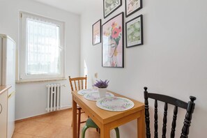 Ein Essbereich mit einem Holztisch, Stühlen, einem Fenster mit floralem Vorhang und Wandbildern.