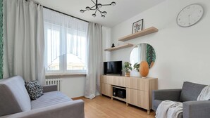 Ett modernt vardagsrum med en soffa, en tv, en spegel och ett fönster med gardiner.