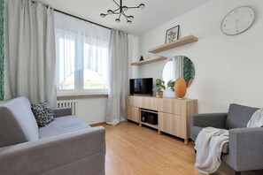 Ein modernes Wohnzimmer mit einer Couch, einem Fernseher, einem Spiegel und einem Fenster mit Vorhängen.