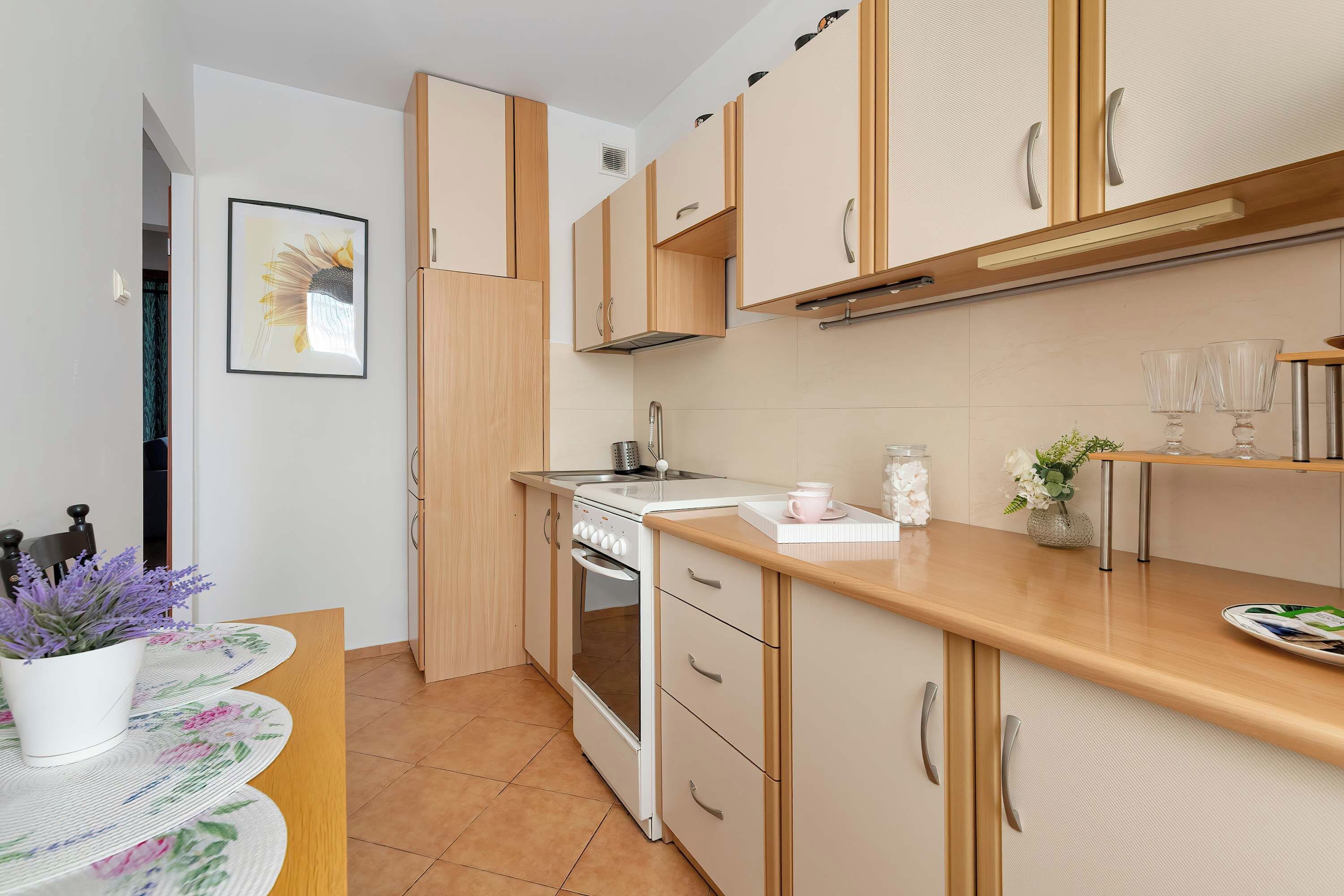 A modern kitchen with wooden cabinets, a built-in oven, and a countertop with a coffee maker and glasses.
