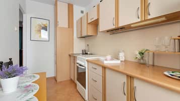 A modern kitchen with wooden cabinets, a built-in oven, and a countertop with a coffee maker and glasses.