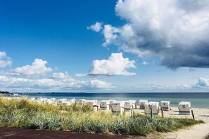 A beach with rows of white chairs, some with numbers on them, and a clear sky with clouds. - Beachfront Quarter at Seehof (Sierksdorf)