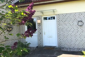 A house with a white door, a brick wall, and a small garden with purple flowers. - Beachfront Quarter at Seehof (Sierksdorf)