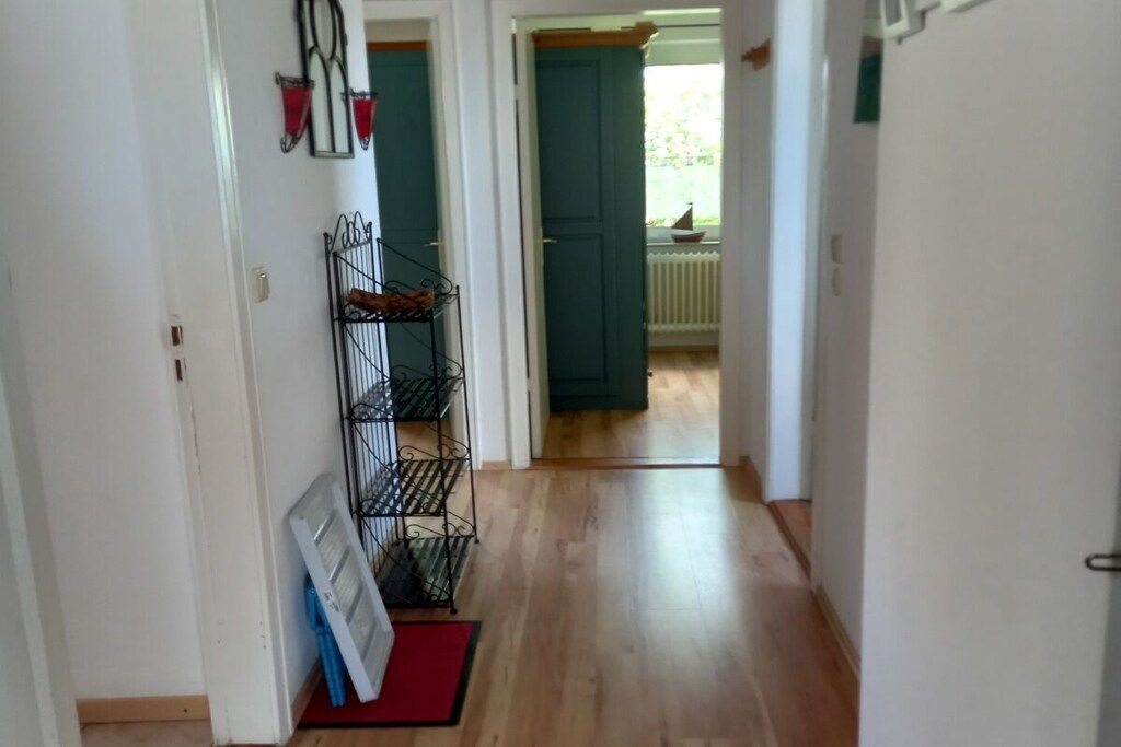 A hallway with a metal rack, a red mat, and a door leading to a room with a window.