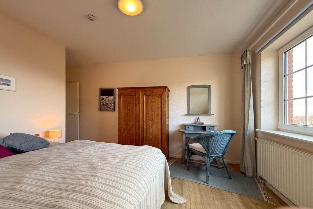 A bedroom with a bed, a desk, a chair, a wardrobe, and a window.