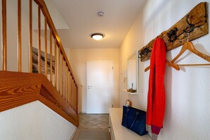 Ein Flur mit einer Holztreppe, einer weißen Tür am Ende und einem Kleiderhaken mit einem roten Kleidungsstück.