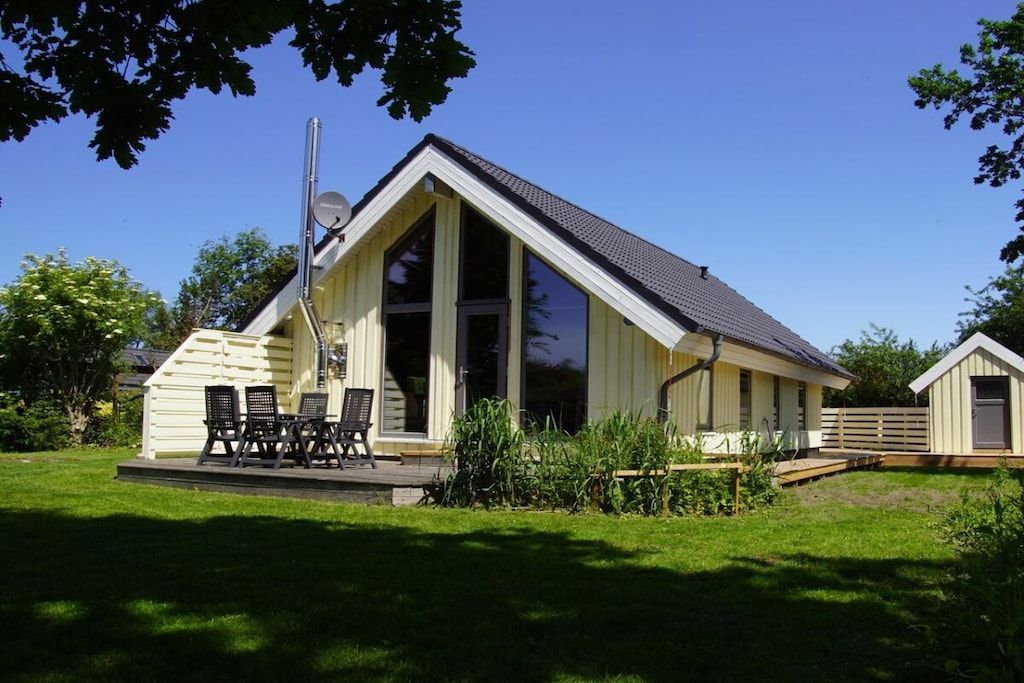 Eingeschossiges Haus mit geneigtem Dach, einer Satellitenschüssel und einer Terrasse mit Gartenmöbeln.