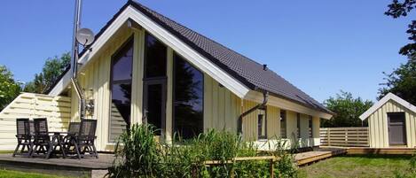 A single-story building with a sloped roof, large windows, and a deck area with outdoor furniture.
