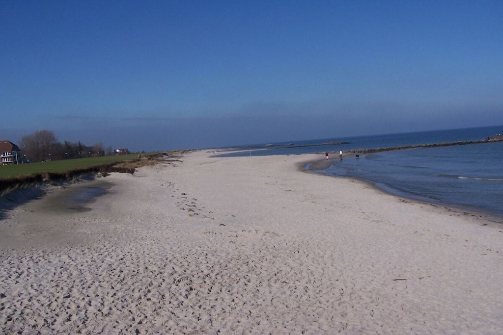 Een zandstrand met een heldere lucht, enkele mensen en een verre kustlijn.