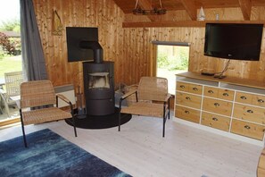 Ett mysigt rum med en vedeldad kamin, flätade stolar, en tv och ett träskåp med lådor.
