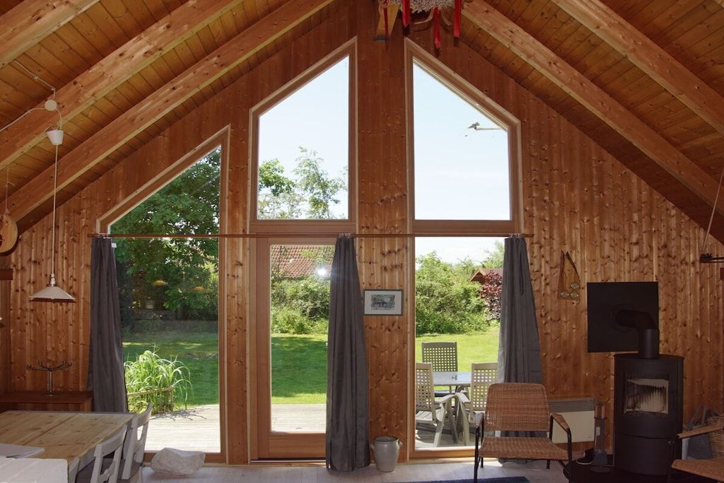 A wooden interior with a high ceiling, a fireplace, and a view of a garden through large sliding doors.