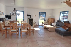 A spacious living area with a dining table, chairs, a sofa, and a television. - Thatched holiday home with lighthouse view (Putgarten)