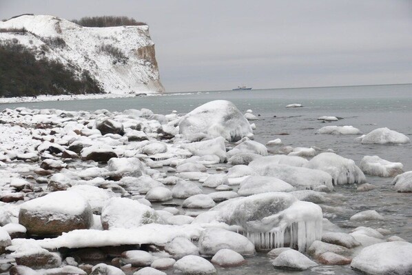 A rocky shoreline with ice formations and a distant ship. - Thatched holiday home with lighthouse view (Putgarten)