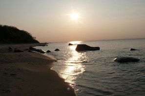 A beach with sunlight reflecting off the water and rocks. - Thatched holiday home with lighthouse view (Putgarten)