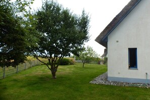 A white building with a blue door, surrounded by a well-maintained lawn and trees. - Thatched holiday home with lighthouse view (Putgarten)