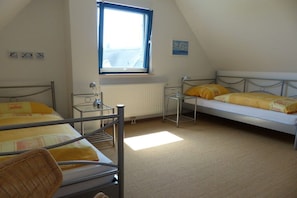 A room with two beds, a window, a radiator, and a small table. - Thatched holiday home with lighthouse view (Putgarten)
