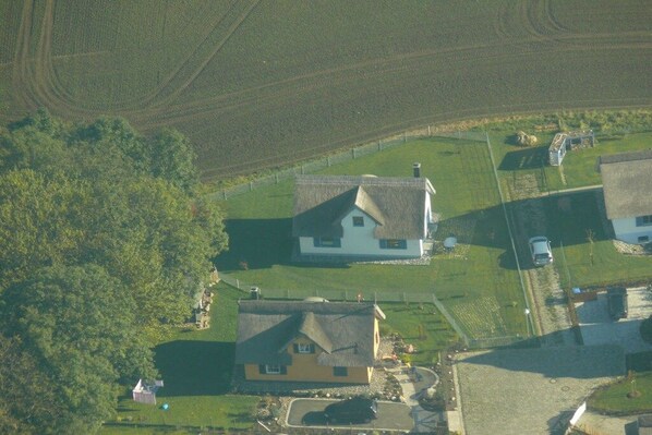 A rural area with two houses, one with a thatched roof and another with a gabled roof, surrounded by fields and a small fenced area. - Thatched holiday home with lighthouse view (Putgarten)