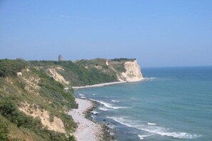 A coastal landscape with a cliff, a beach, and a tower. - Thatched holiday home with lighthouse view (Putgarten)
