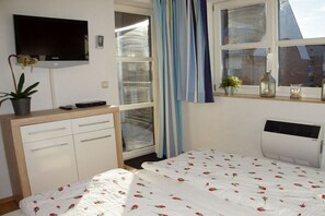 A bedroom with a bed, a TV, a window with curtains, a radiator, and a potted plant. - Holiday apartment with 2 bedrooms (Schönberger Strand)
