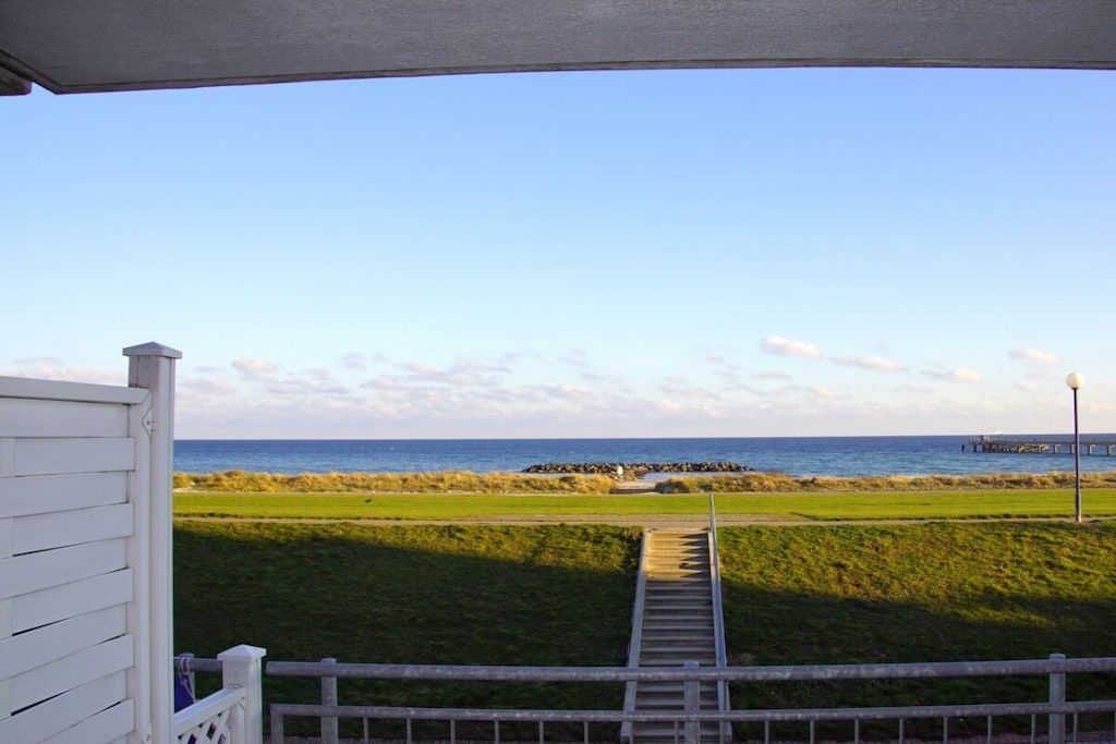 A pathway leading to a beach with a clear view of the ocean and a pier in the distance.