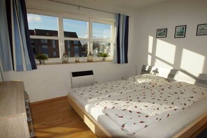 Ein Schlafzimmer mit einem großen Bett, einem Fenster mit Vorhängen, einem Nachttisch und einem Wandheizkörper.