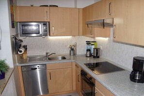 A compact kitchen with a dishwasher, microwave, stove, and coffee maker. - Holiday apartment with 2 bedrooms (Schönberger Strand)