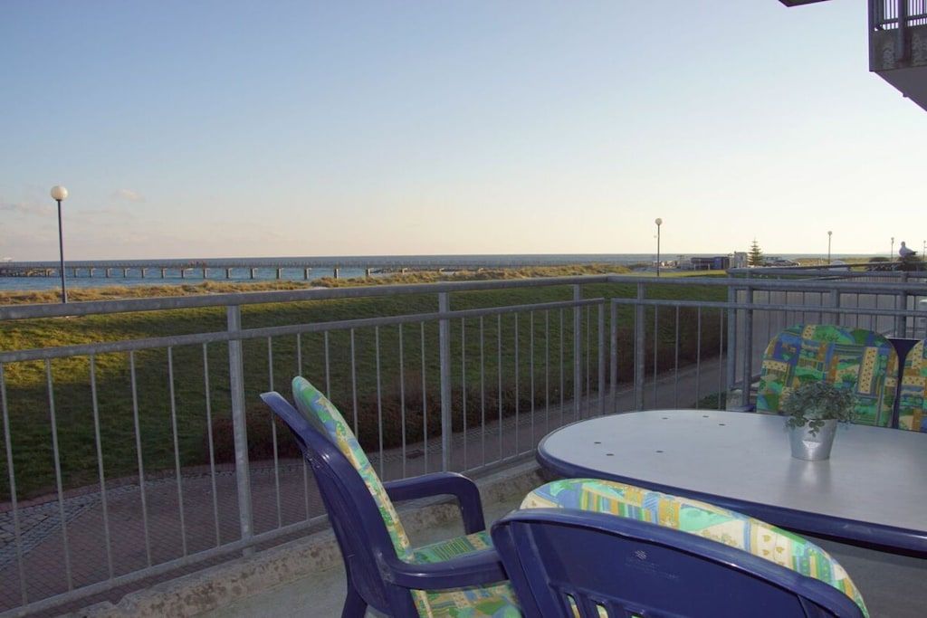 Uma varanda com vista para o mar, uma mesa e cadeiras.