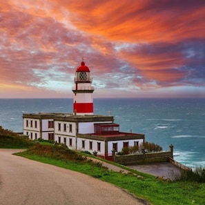 Un faro con la parte superior roja, el cuerpo blanco y un pequeño edificio contiguo con techo rojo.