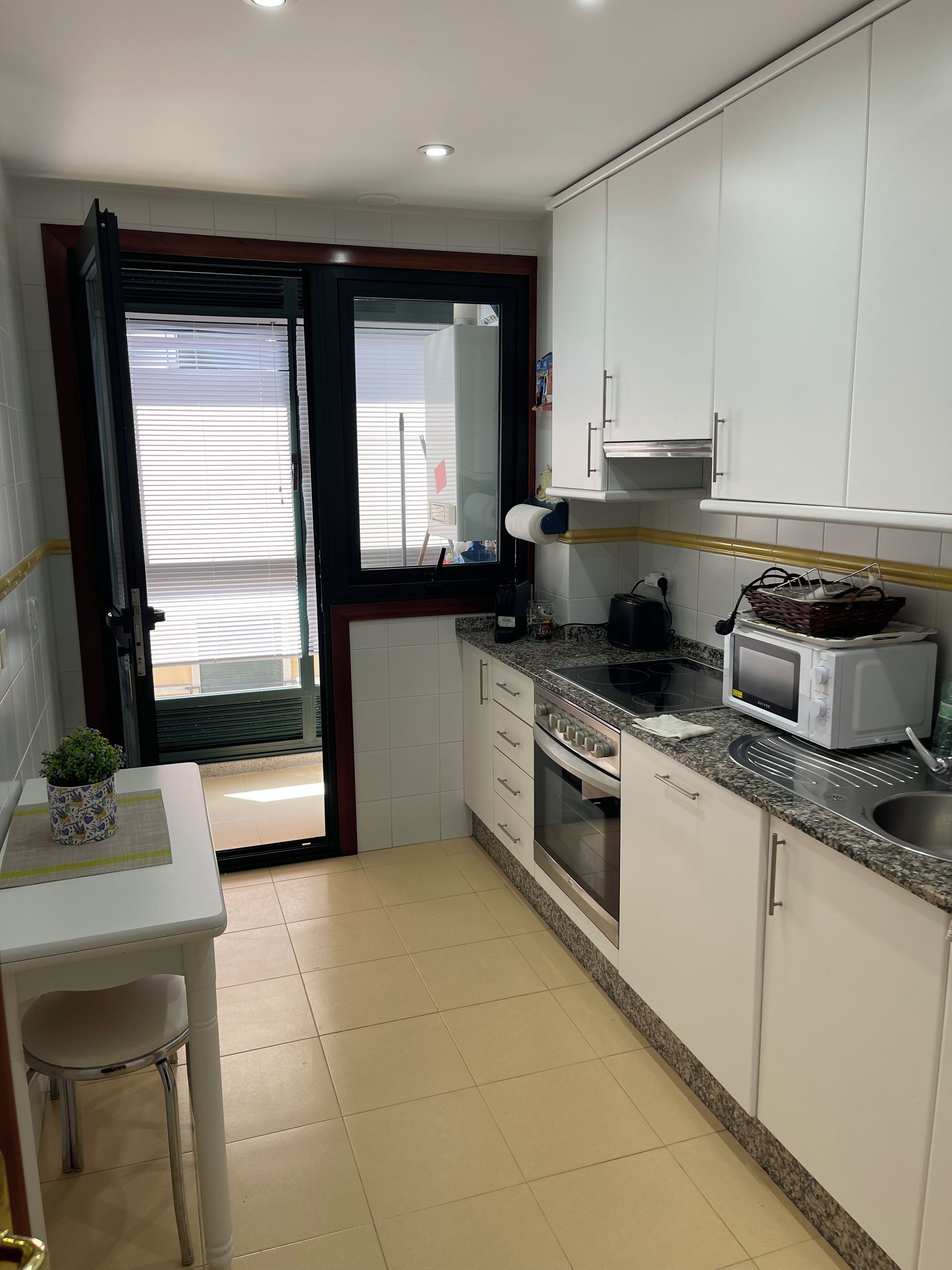 Cocina compacta con gabinetes blancos, microondas, estufa y lavamanos.