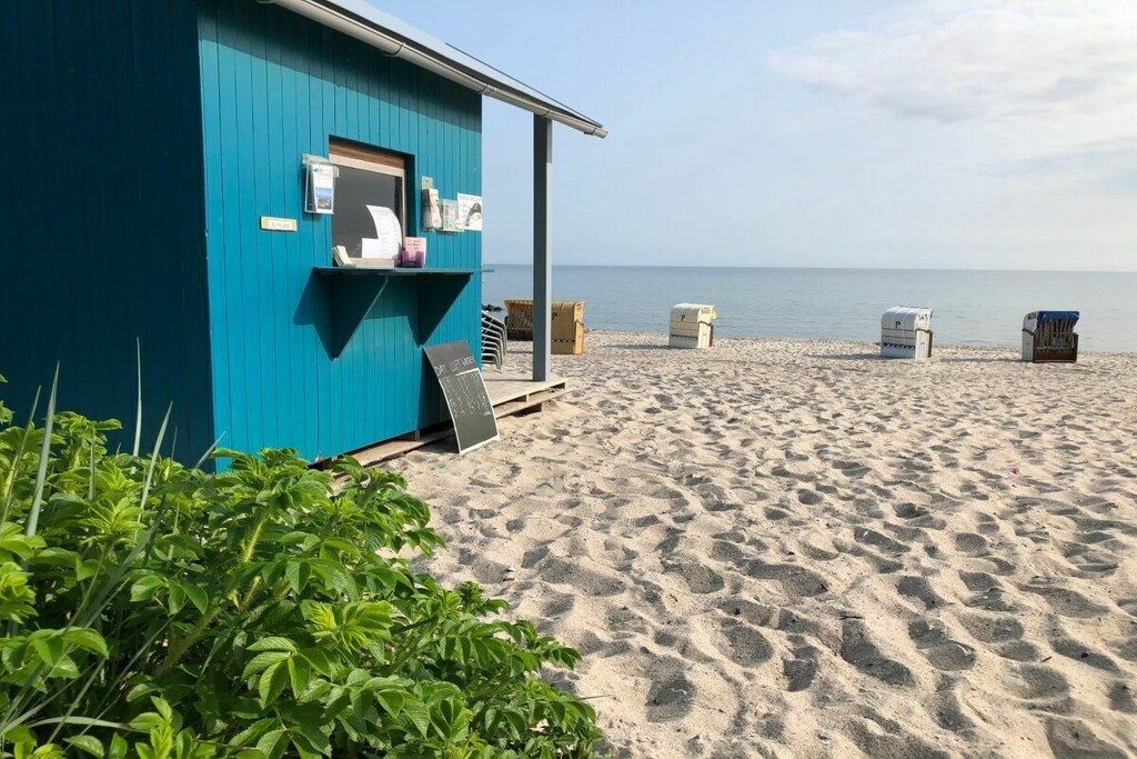A beachside shack with a small porch and a signboard, surrounded by sand and a clear sky.