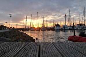A marina with multiple boats docked, a wooden pier, and a sunset in the background. - Holiday home in Hohwacht with swimming pool (Hohwacht)