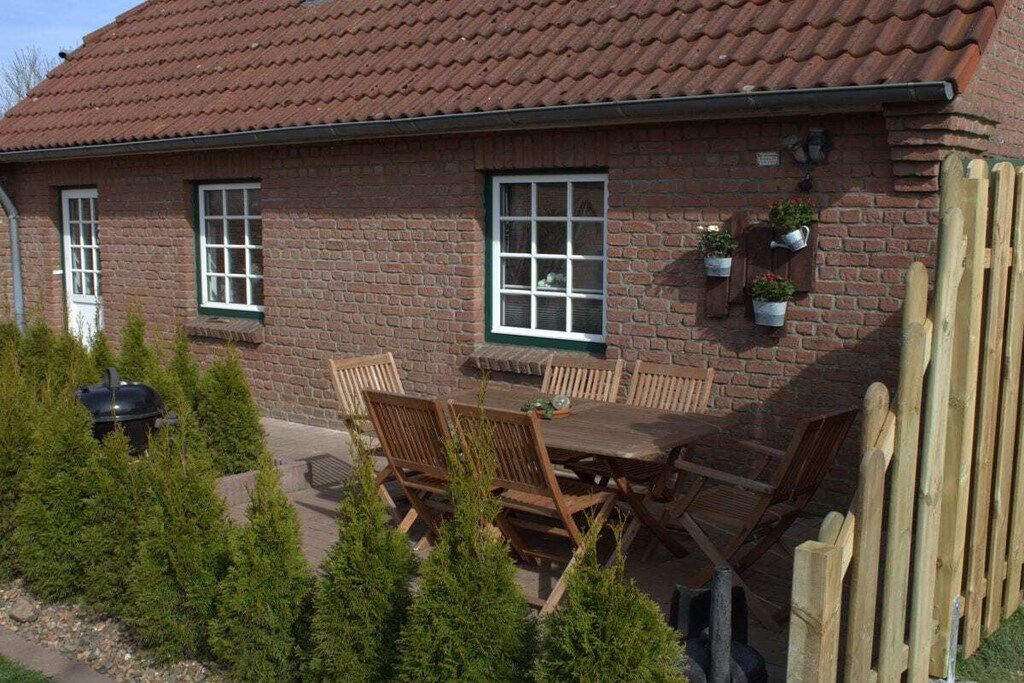 A brick house with a tiled roof, a patio with wooden furniture, and potted plants.