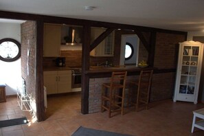 A kitchen with a brick wall, wooden beams, a bar area with stools, and a white cabinet with glass doors. - Holiday apartment with 1 bedroom (Ahrenviöl)