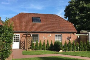 A two-story brick house with a tiled roof, a front door, and a small window. - Holiday apartment with 1 bedroom (Ahrenviöl)