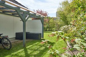 A covered outdoor area with a bicycle, a white building, and a garden with various plants. - Baltic Sea holiday home Scharbeutz (Scharbeutz)