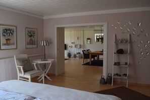A bedroom with a bed, a chair, a small table, a lamp, and a view into the dining area. - Tanja's Baltic Sea dream home (Lütjenburg)