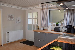 A modern kitchen with a built-in stove, a window with curtains, and a radiator. - Tanja's Baltic Sea dream home (Lütjenburg)