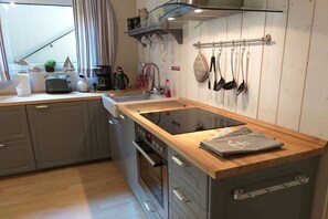 A kitchen with a wooden countertop, a built-in oven, and a wall-mounted rack with kitchen utensils. - Tanja's Baltic Sea dream home (Lütjenburg)