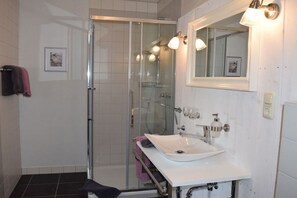Ein Badezimmer mit einer Duschkabine, einem weißen Waschbecken und einem Spiegel mit Wandleuchten.
