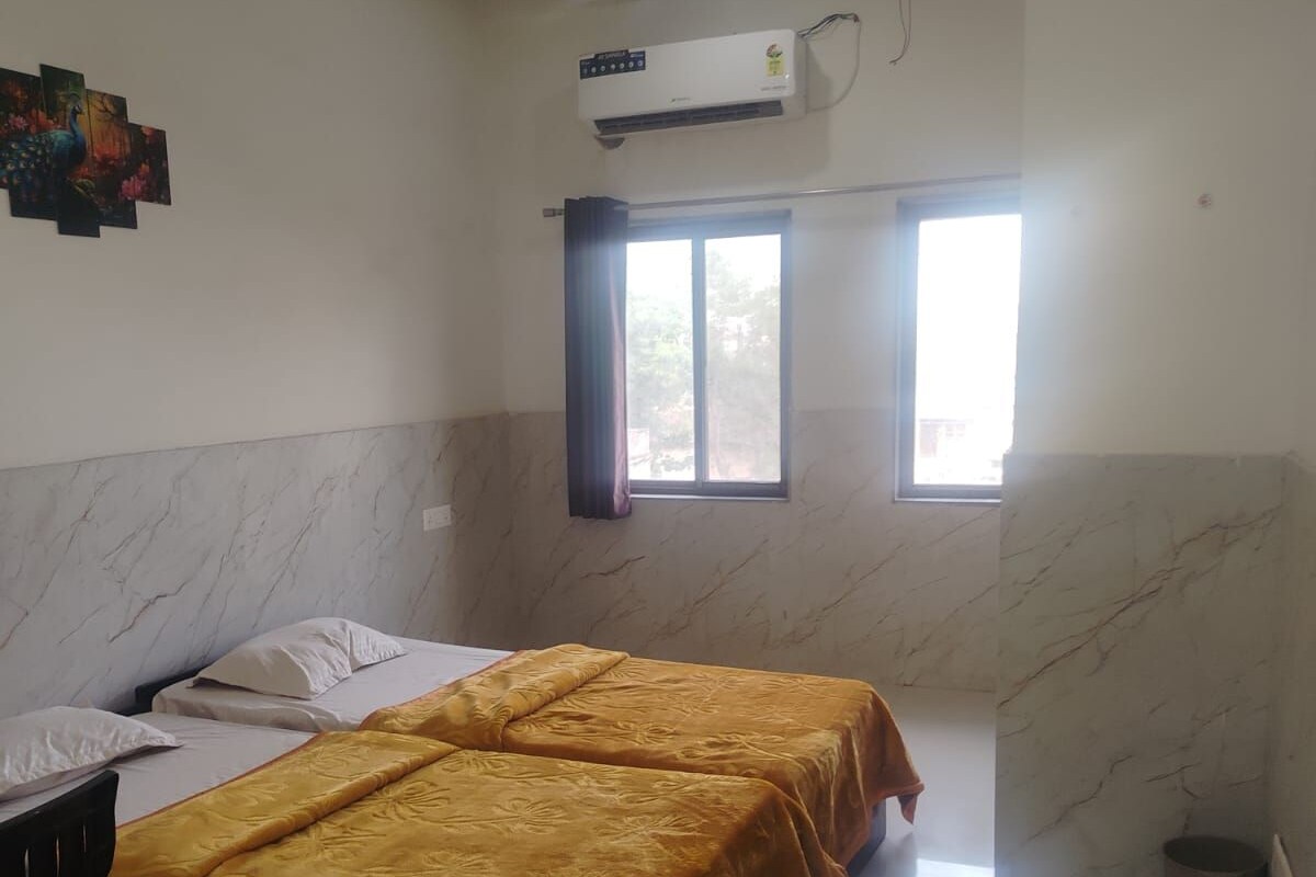 Una habitación de hotel con cama, ventilador de techo, equipo de aire acondicionado y ventana con cortinas.