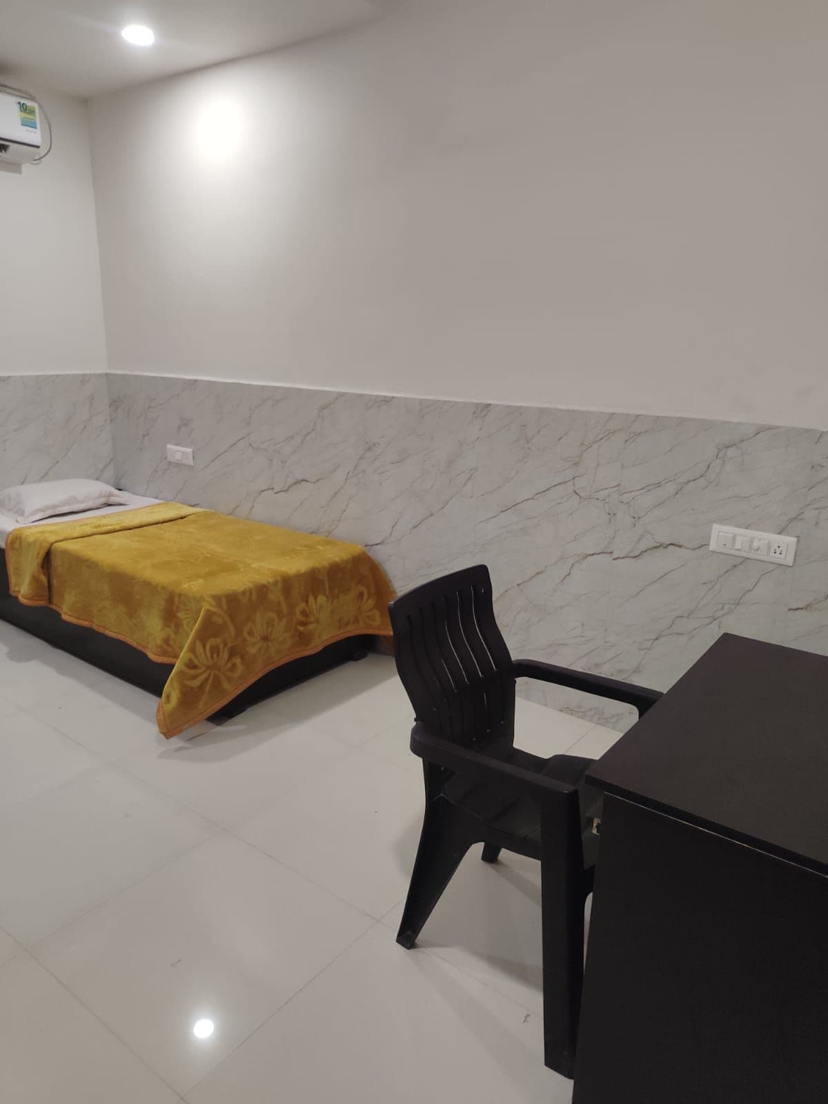 Habitación de hotel con cama, una silla, una mesa y una pared de mármol.