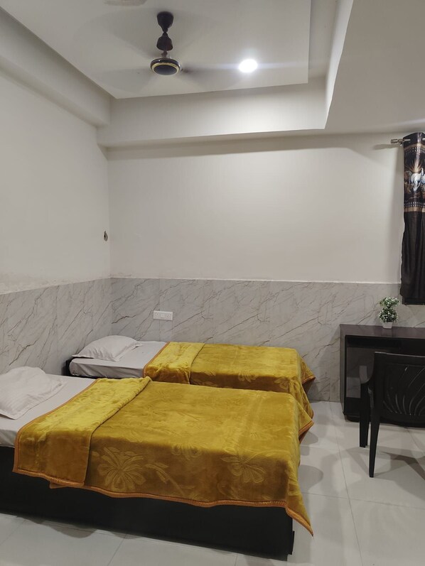 A room with two beds, a desk, a chair, a ceiling fan, and a wall-mounted light fixture.