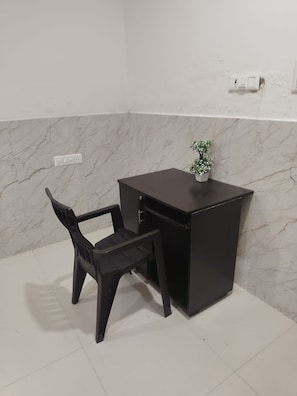 A small, dark-colored desk with a chair in front of it, a potted plant on the desk, and a marble-patterned wall.