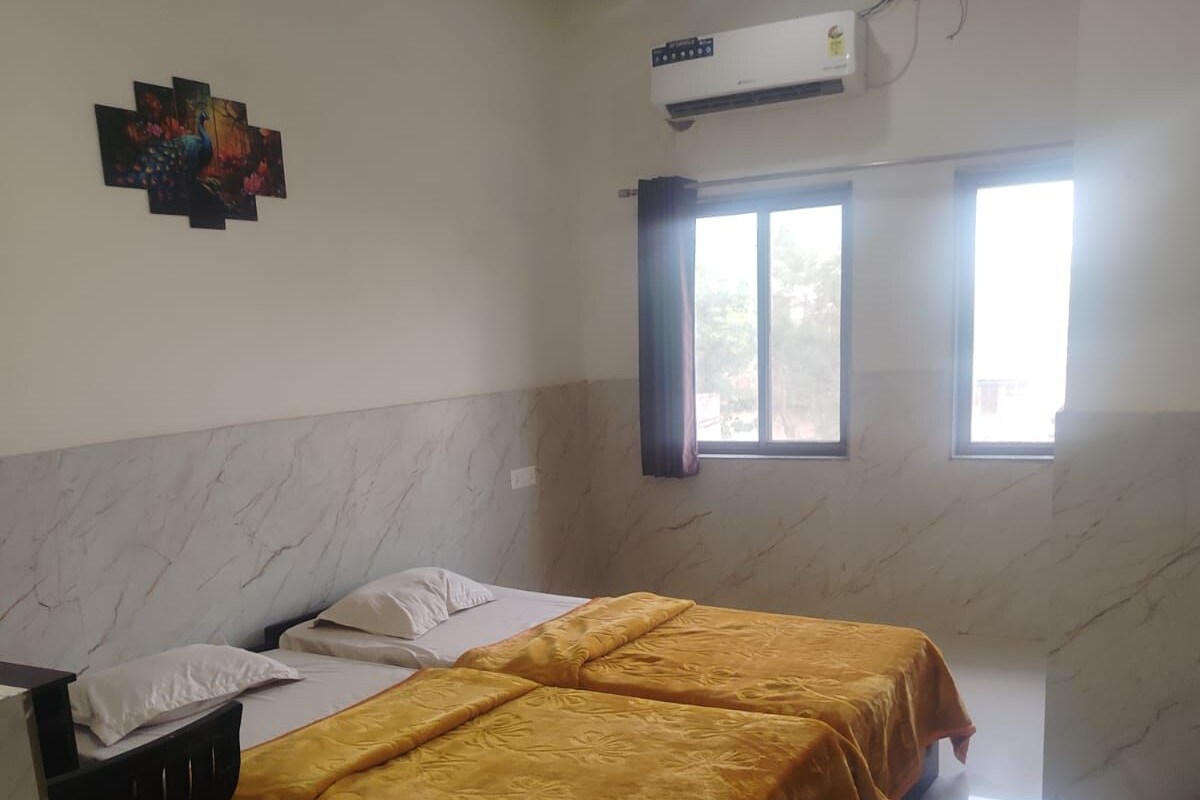 Una habitación con dos camas, un escritorio, un equipo de aire acondicionado y un ventanal con cortinas.