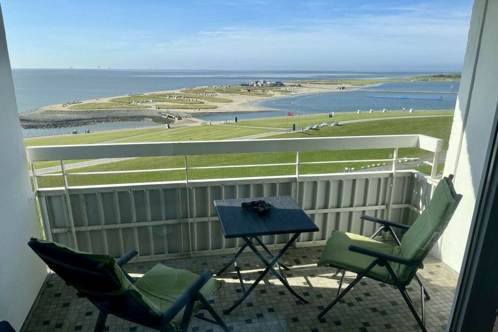 Un balcon avec deux chaises et une petite table, donnant sur une zone côtière avec une plage et l’eau.